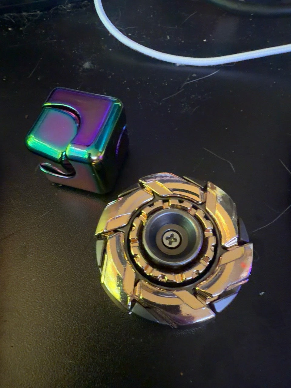 Daniel’s iridescent metal fidget cube beside a mechanical metal spinner.