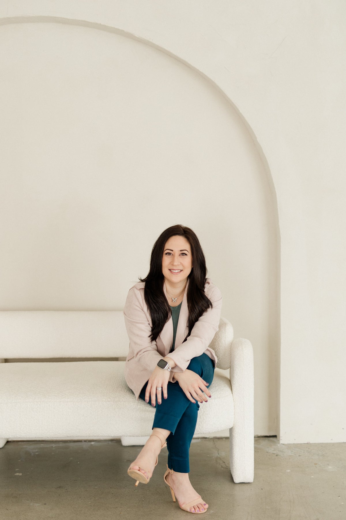 Laura Petix seated on a cream sofa beneath an arched wall, smiling at the camera.