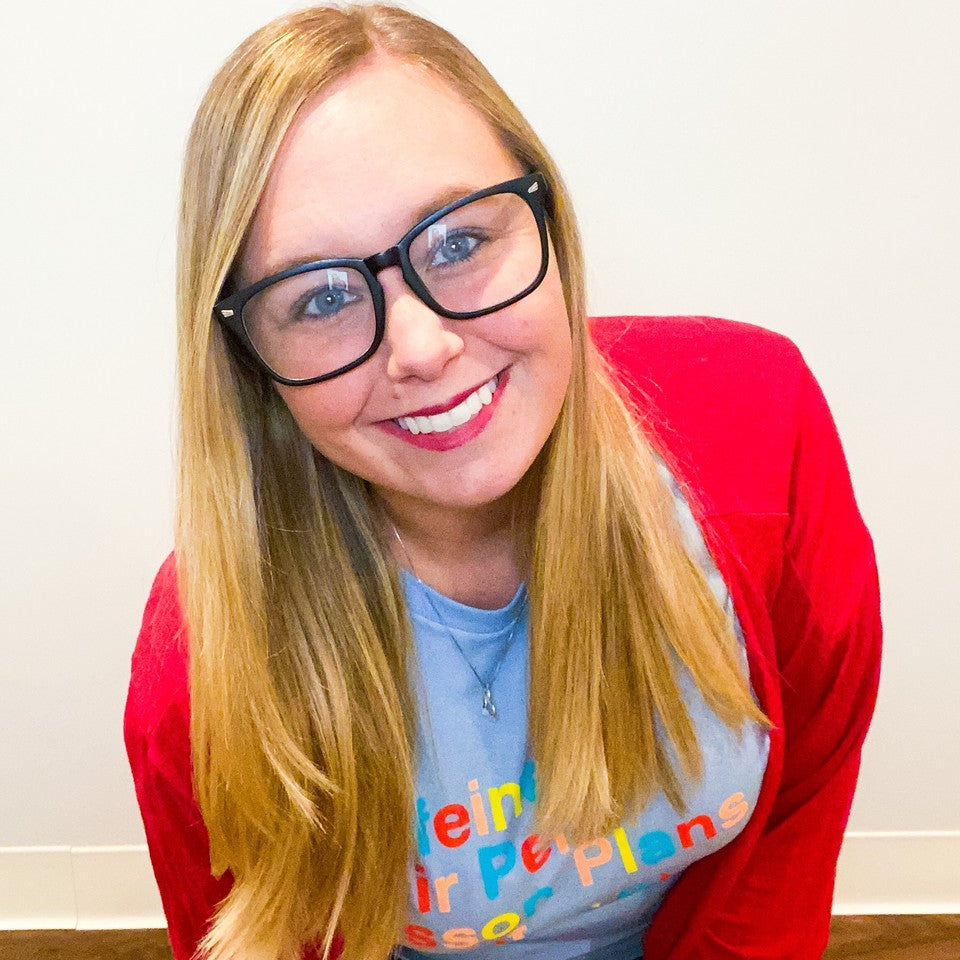 Portrait of Heather Cacioppo smiling, wearing black glasses and a red cardigan.