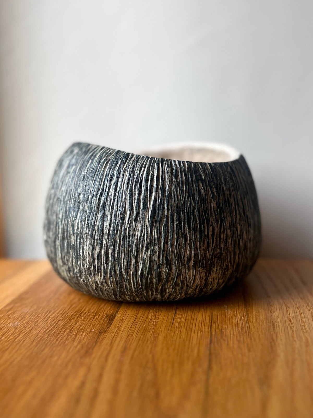 A rounded Swoop Sgraffito paper-pulp bowl with a wavy rim, dark exterior and light scratched lines, on a wooden surface.