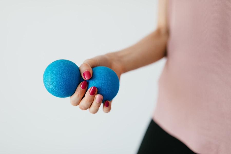A hand holds a textured blue, peanut-shaped squeeze ball against a pale background.