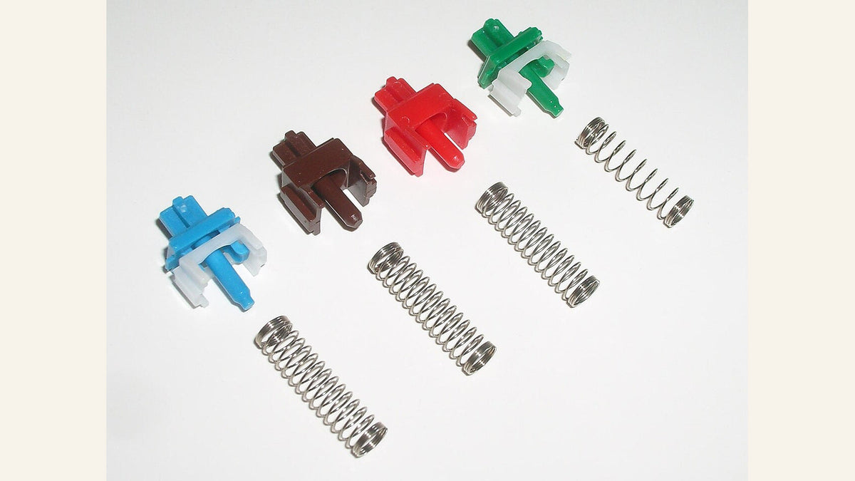 Blue, brown, red and green Cherry MX switch stems with coil return springs arranged on white.