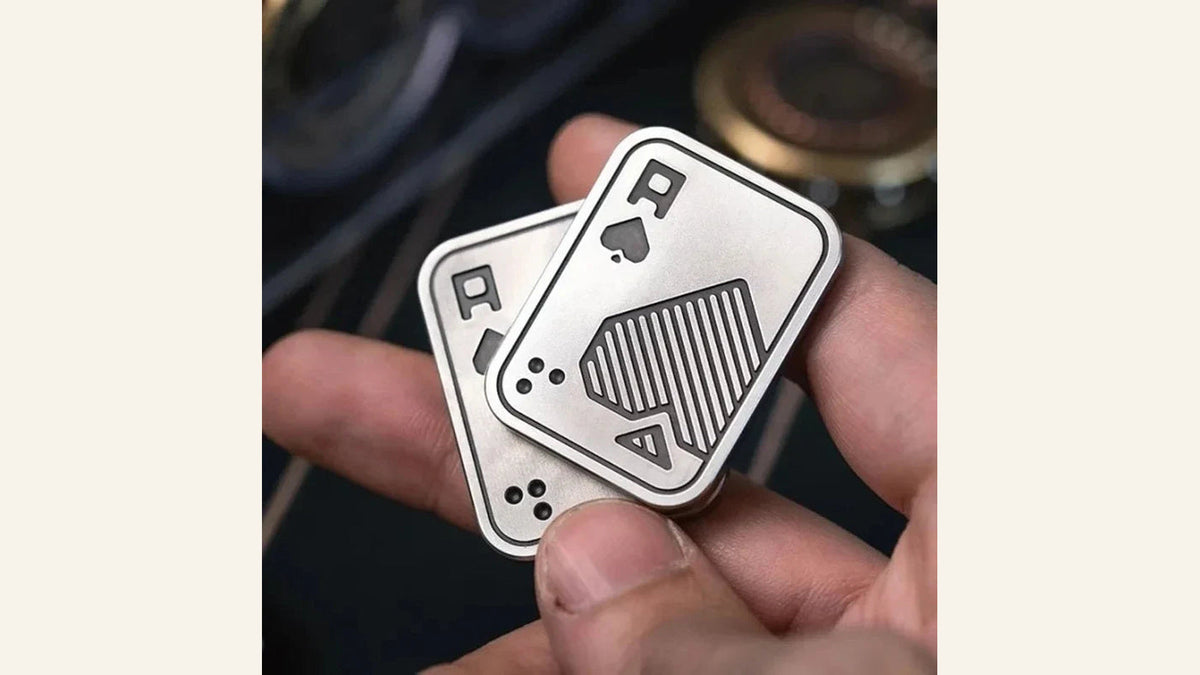 A hand holding two silver-colored Ace-of-spades-pattern slider plates.