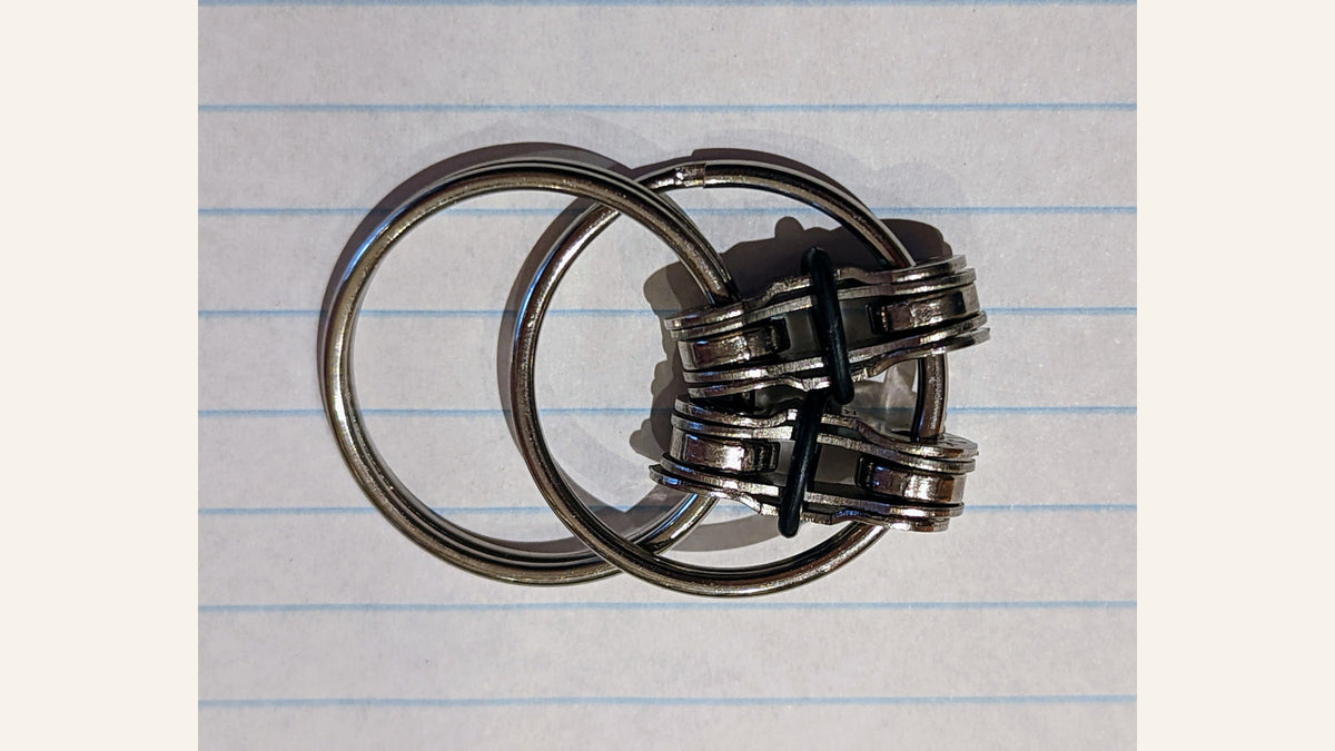 Bike-chain-style fidget made from linked metal rings and chain plates on lined paper.
