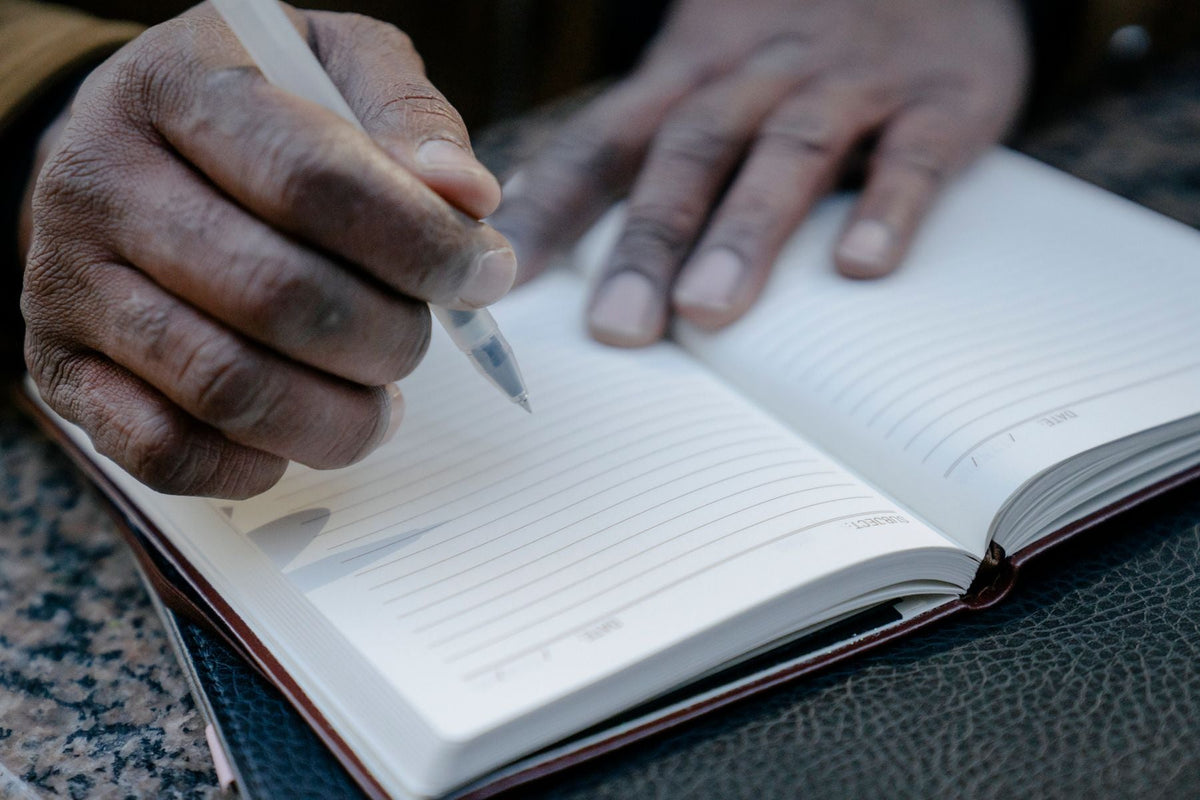Hands write notes with a pen in an open notebook on a desk.