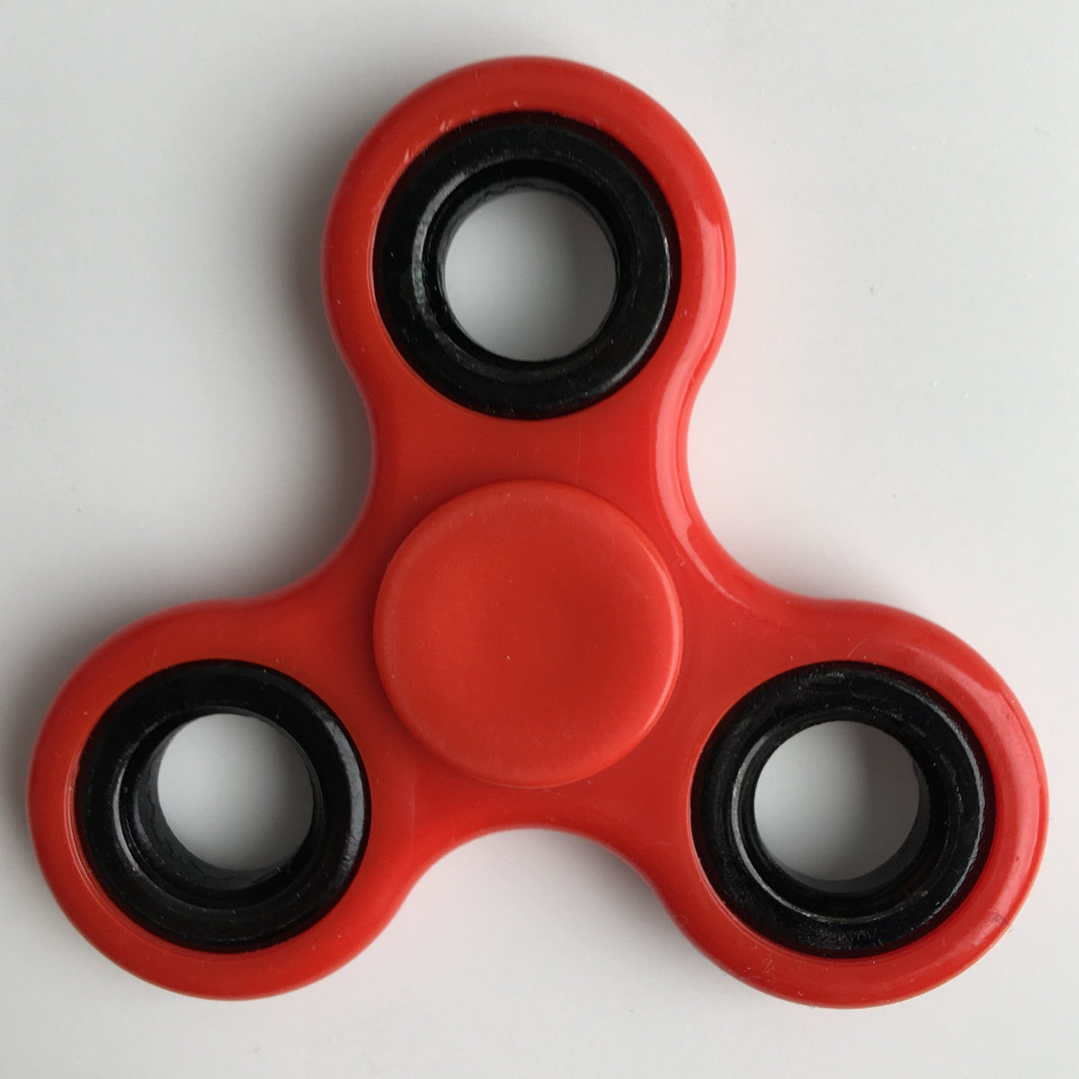 Red three-arm fidget spinner with black center grip and metal bearings.