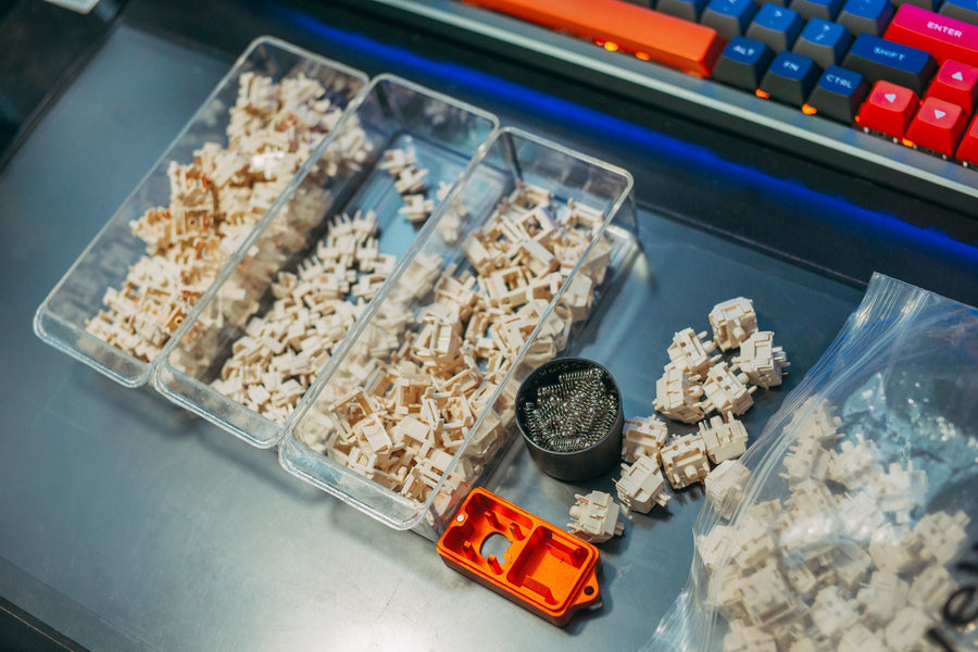 Clear storage boxes hold keyboard switches and small metal springs on a desk.