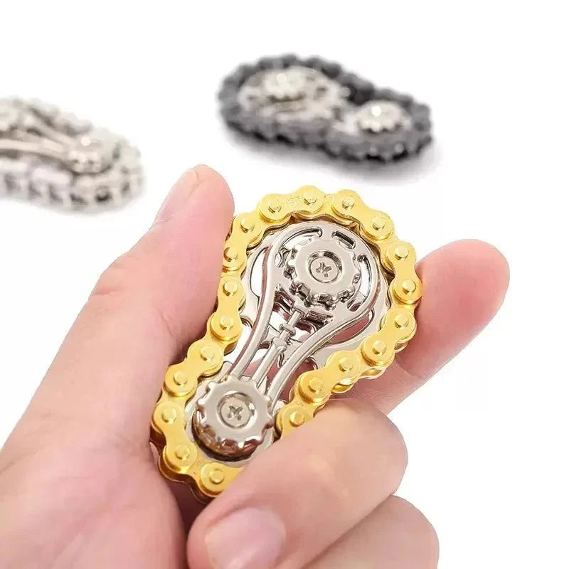 Hand holding a gold-tone chain-style metal fidget spinner, with silver and black versions in the background